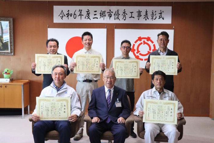 表彰式の集合写真で、前列は受賞者2名と中央に市長、後列は受賞者4名