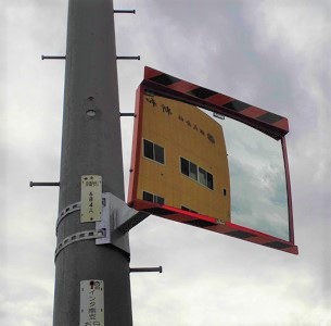 電柱に設置された市の道路反射鏡に、オレンジ色の建物が映っている写真