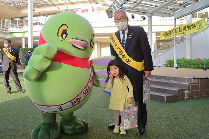 ららぽーと新三郷のスカイガーデンで、かいちゃんと黄色いたすきをつけた三郷市長とピースサインをしている女の子の記念写真