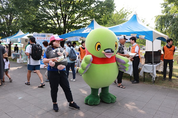 テントが建ち並ぶ屋外のイベント会場でかいちゃんとつぶちゃんが来場者を迎え入れている写真