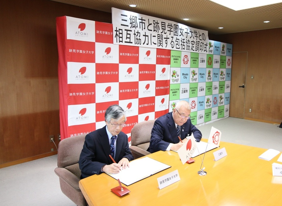 調印式で、木津雅晟市長と山田徹雄学長が協定書にサインをしている写真