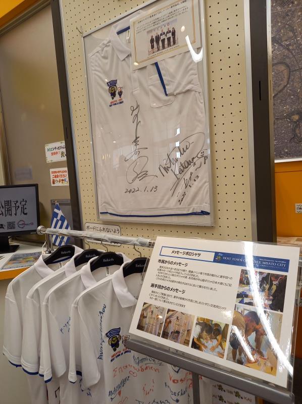 掲示板にサイン入りTシャツが入った額縁が貼られ、手前のハンガー掛けにTシャツが掛けられている写真