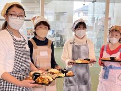 三角巾にエプロンを着用した4名の女性が完成したギリシャ料理をそれぞれ手に持っている写真