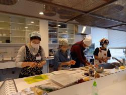 三角巾にエプロンを着用した4名の参加者が包丁で食材をカットしている様子の写真