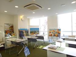 6台の長机が設置され、室内奥の壁側と窓ガラス側に4枚の絵画の作品が展示されている写真