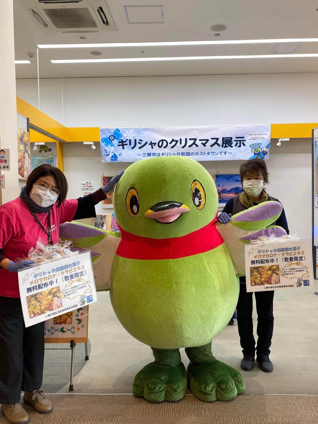 クリスマス展示を行っているブースにお手伝いに来た三郷市マスコットキャラクターかいちゃんと2名の女性スタッフの写真
