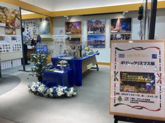 壁にギリシャのクリスマス風景のパネルが飾られた展示ブースの写真