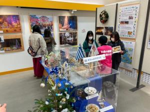ギリシャのクリスマス展示ブースに来場したお客さんに女性スタッフが焼き菓子を配布している様子の写真