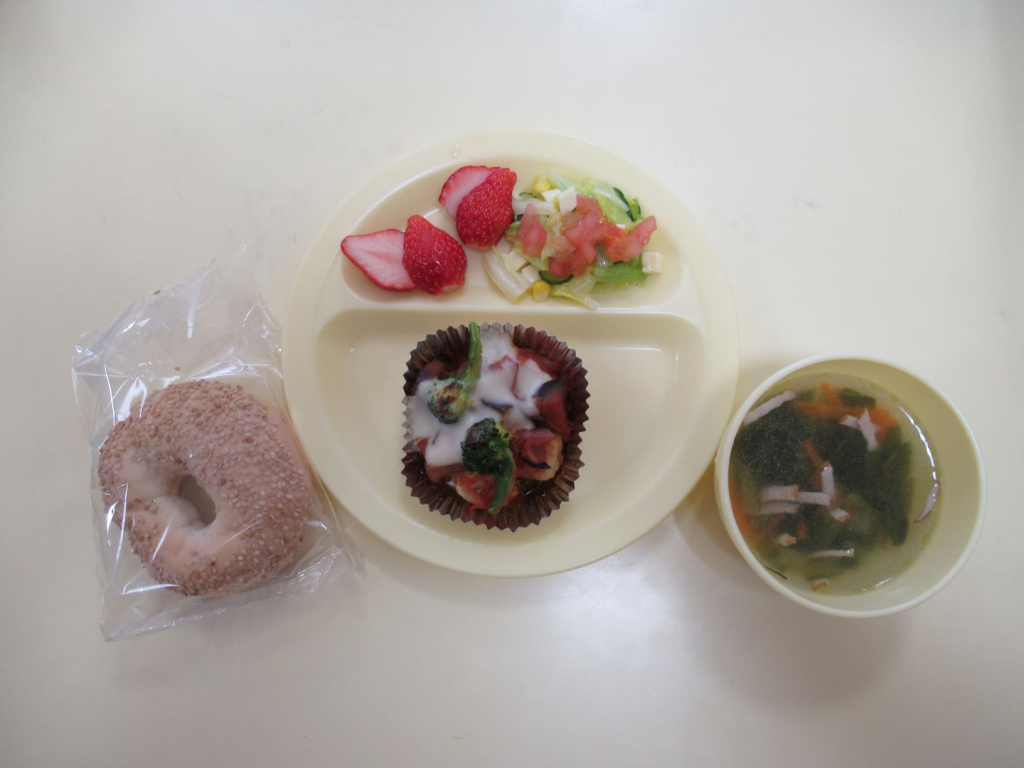 給食トレーにスズカキアのクリーム焼き、グリークサラダ、いちご、フルーツギリシャヨーグルトが盛り付けられ、スープカップに入ったみさと小松菜スープ、透明の袋に入ったギリシャパンクルーリーが添えられた保育所のギリシャ給食の写真