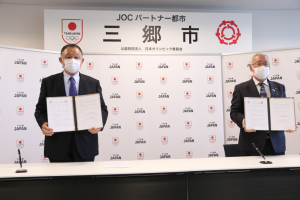 JOCの山下泰裕会長と市長がそれぞれ協定書を広げ両手で持って立っている写真