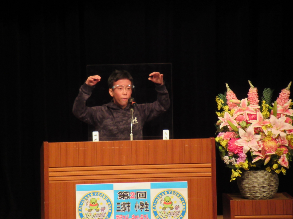 檀上で両手を上げて発表している、前間小学校6年西山蒼真さんの写真