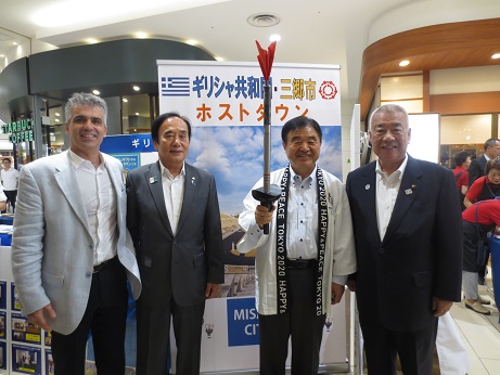 ホストタウンのイベントコーナーで、木津市長や駐日ギリシャ大使館 参事官、埼玉県知事がトーチを持ったオリンピック組織委員会副会長と一緒に並んで記念撮影をしている写真