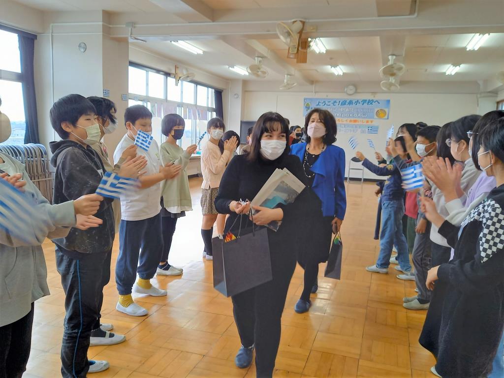 2列に並んで向かい合うように立ち拍手で出迎えている児童達の間を木戸教授とエフィさんが歩いている写真