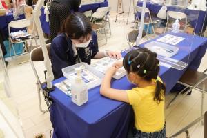 クラフト体験ブースで黄色の服を着た女の子が女性スタッフに教わりながら体験を行っている様子の写真