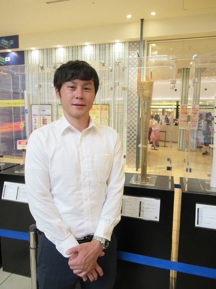 展示された金色のトーチの横に立ってにこやかな表情で記念撮影をする渡邉一樹氏の写真