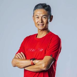 赤色のシャツを着て腕組みした竹谷賢二氏の上半身の写真