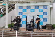 屋外のイベント広場で高校生の軽音楽部の4名が演奏を行っている様子の写真
