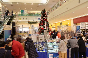 大きなクリスマスツリーが設置された商業施設の広場で開催されたギリシャ物産展で大勢のお客さんが買い物ををしている様子の写真