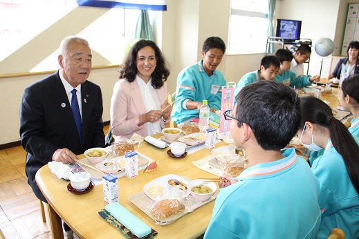 駐日ギリシャ大使夫人と木津市長が、生徒たちとテーブルを囲んで交流しながら給食を食べている写真