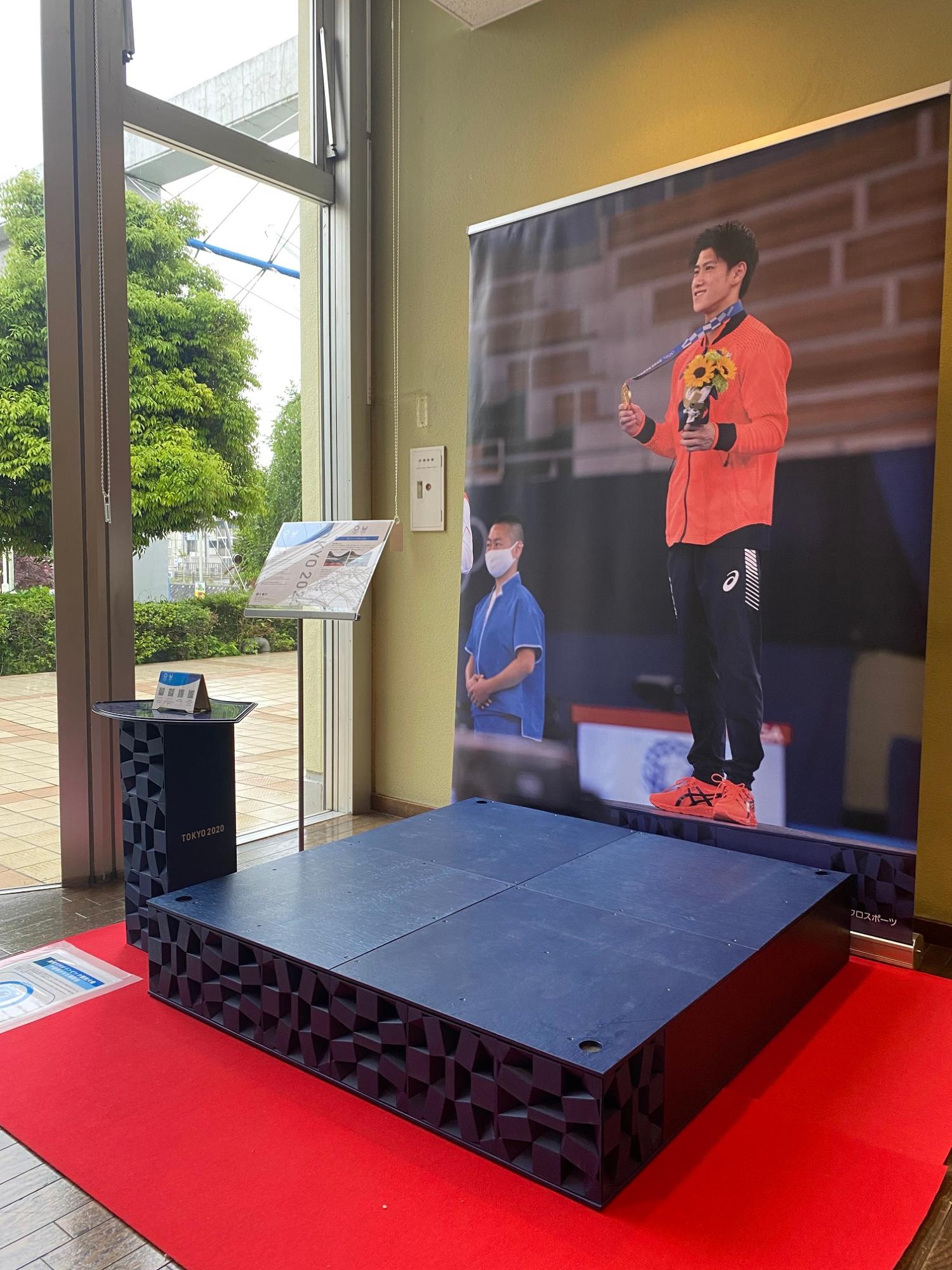 表彰台が設置された後ろの壁に金メダルを獲得した橋本大輝選手が表彰台に登壇した時の写真を背景に設置したフォトコーナーの写真