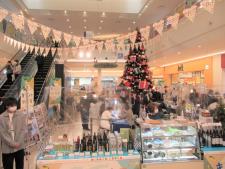 エスカレーター横の広場に大きなクリスマスツリーが設置され周囲に特産品が並んでいるギリシャ物産展の様子の写真