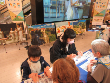 ギリシャの絵画が展示されている前に設置された体験ブースで母親と男の子の親子が体験している様子の写真