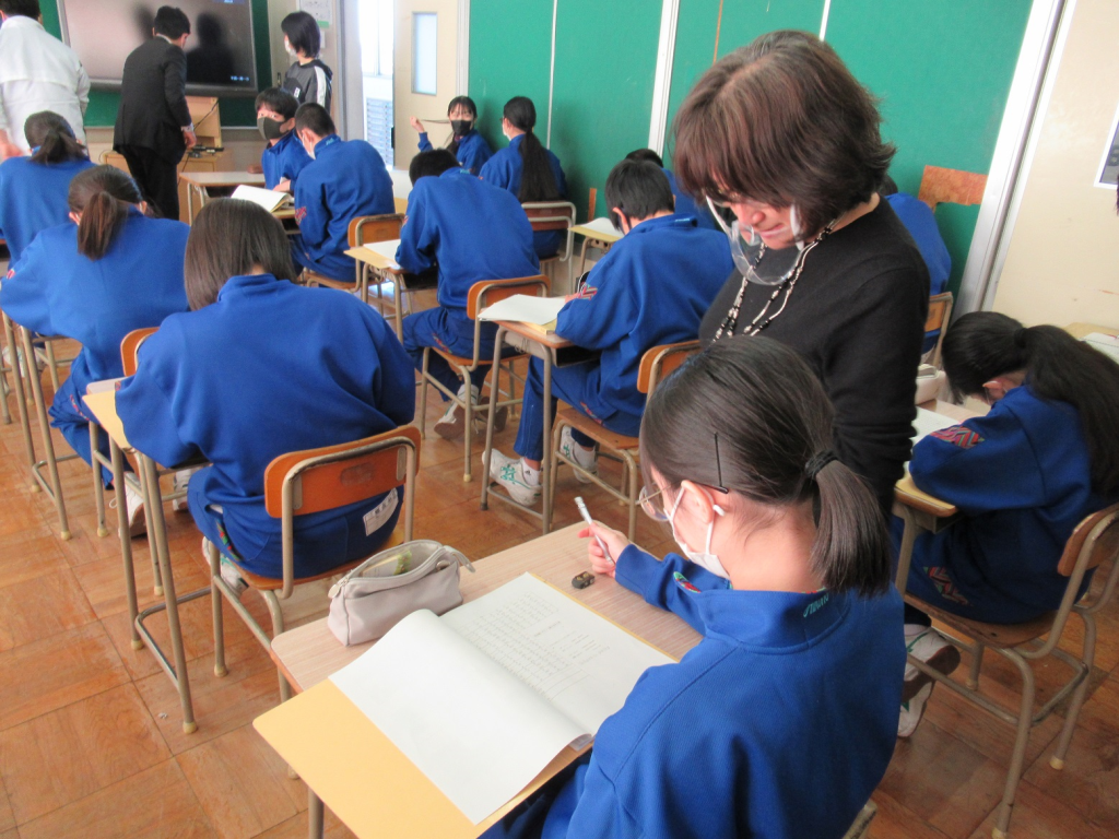 着席した女子生徒の席の右側に立っている女性教師の写真