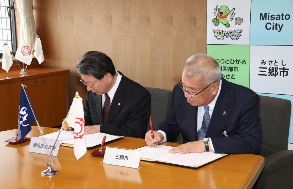 木津雅晟市長と稲葉憲之学長が協定書にサインをしている写真