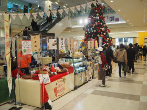 ようかんなどの特産品のお菓子が販売されている観光物産展の販売ブースの前で立ち止まって商品を見ている女性のお客さんの写真