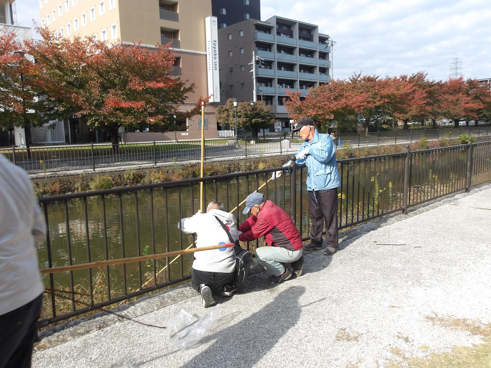 川の浮遊ゴミを網のついた長い棒を使って拾っている写真