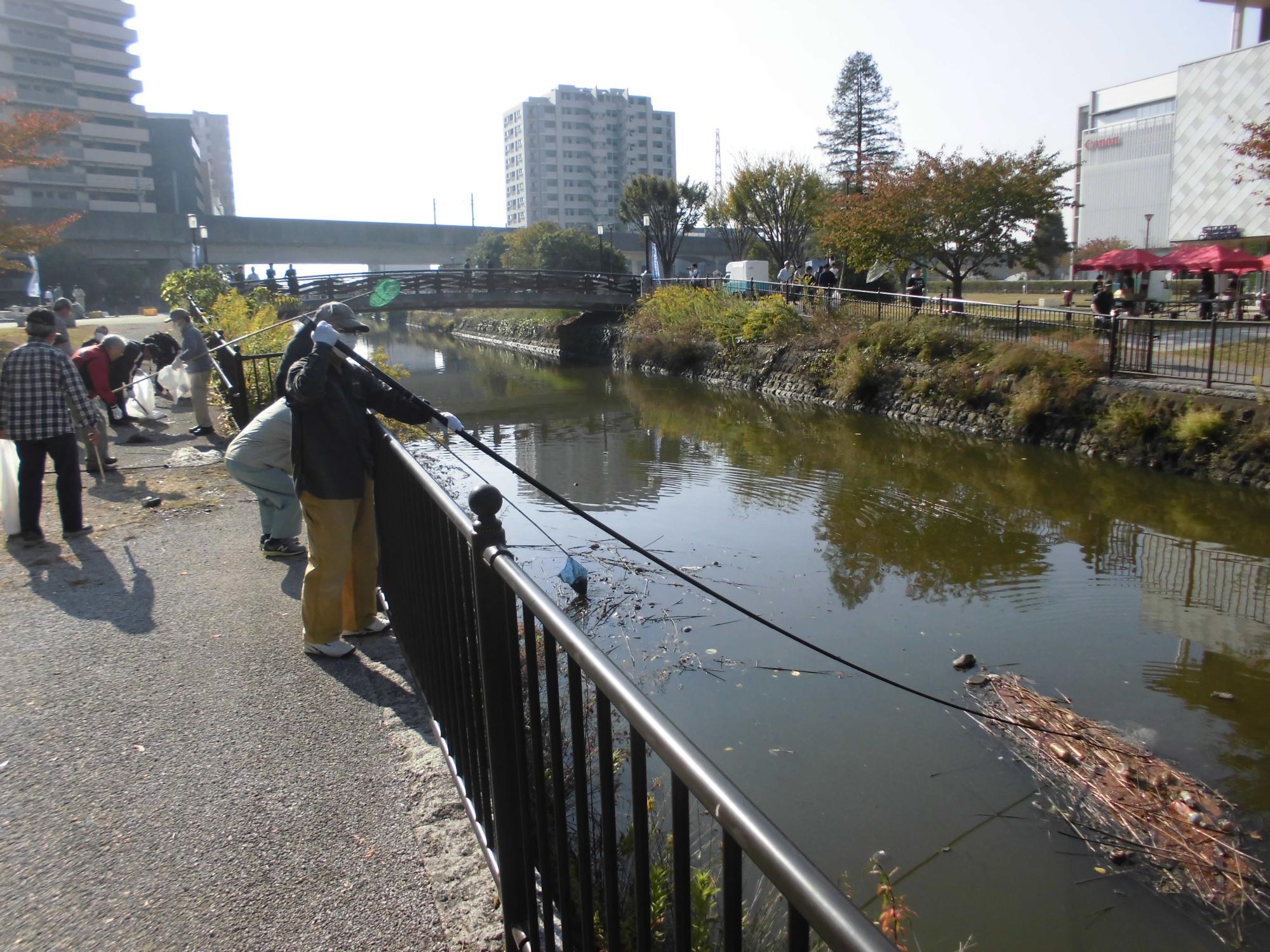 川の浮遊ゴミを網のついた長い棒を使って拾っている写真