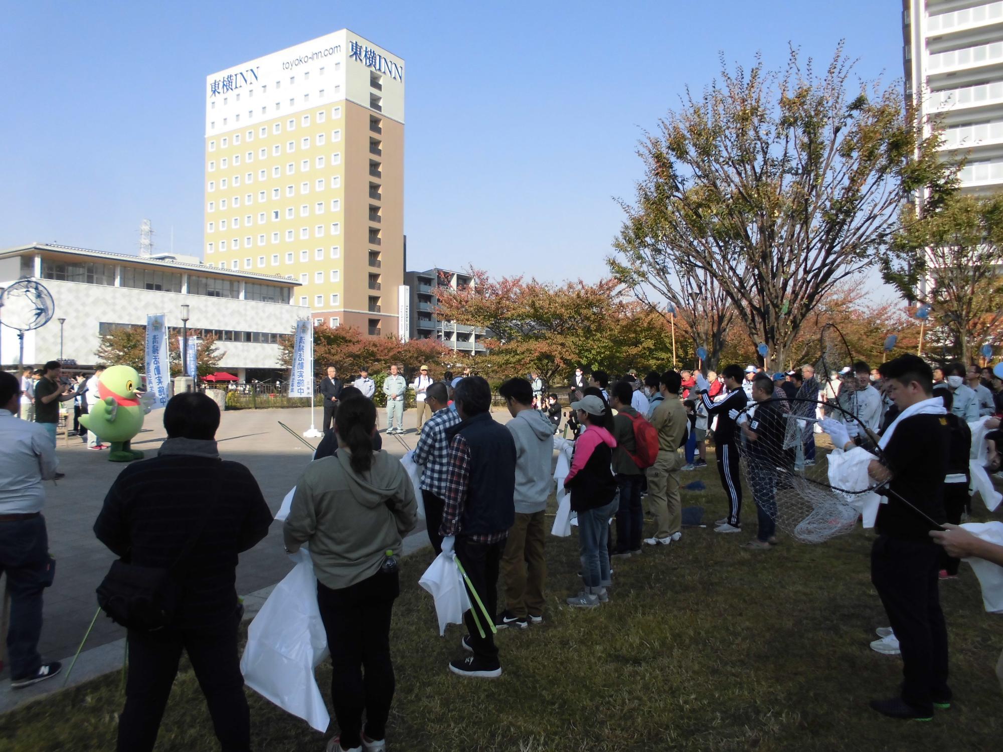 複数の人達が公園の広場に集まり、開会式が行われている写真