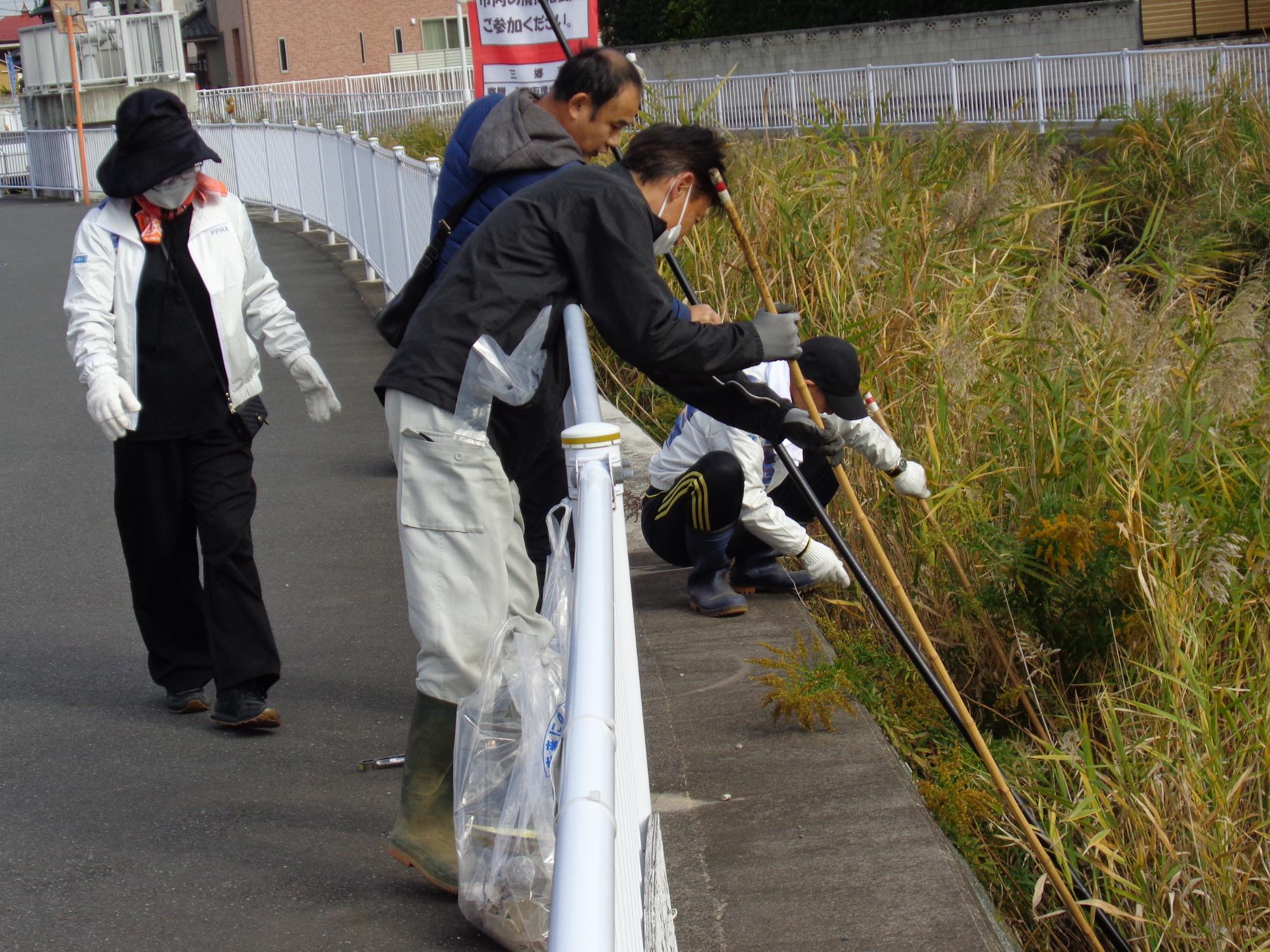 拾ったゴミ入れた袋を持って川沿いを歩いている人達の写真