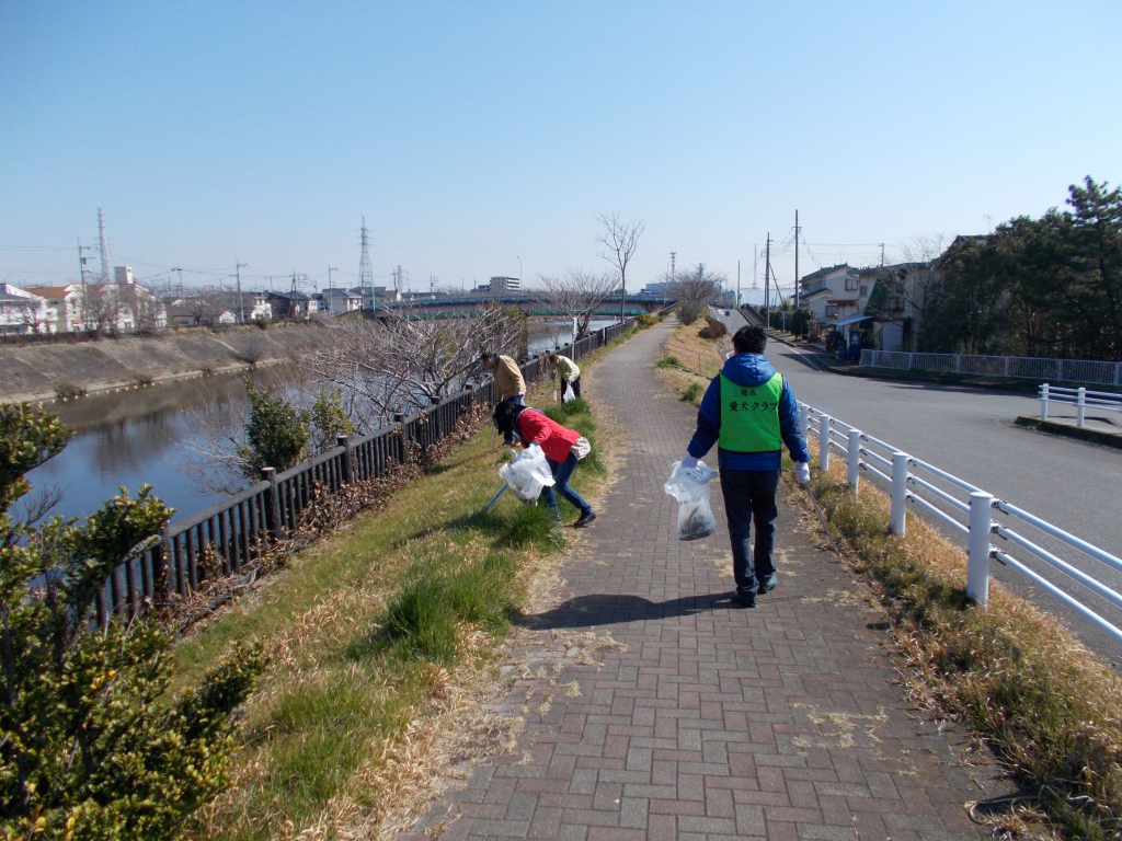 ごみ袋を持ち愛犬クラブの方々が河川敷近くの清掃活動をしている写真