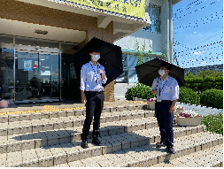 2人の男性が入口前で黒い日傘をさして立ち話をしている写真