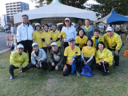 10名程が同じ黄色い服を着た、イベントに参加した会員15名のテントの前で撮影された記念写真