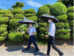 晴天の下、2人の男性が黒い日傘をさして話しながら歩いている写真