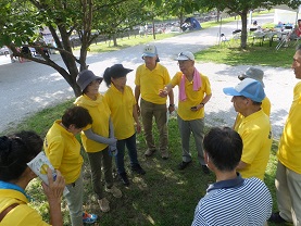 同じ黄色い服を着た会員の方々が木陰で輪になって話をしている様子を上から撮影した写真
