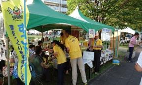 イベントブースに来場者の方が沢山訪れ、黄色いポロシャツを着たスタッフの方々が忙しく対応している様子の写真