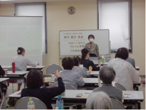 前方に置かれたホワイトボードの前に立ち、マイクを使い話をする講師の先生と席について話を聞く参加者の方々を広報から撮影した写真