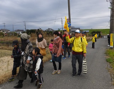 黄色い上着を着た会員が旗を持って歩き、その周りを参加者の方々が歩いている様子の写真