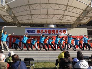 お祭りの舞台で水色のお揃いのTシャツを着た参加者の人達が健康体操をしている様子を写した写真