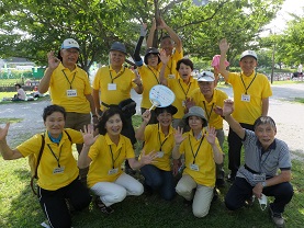 木陰に集まり笑顔で手を挙げている11名の会員の方々の記念写真