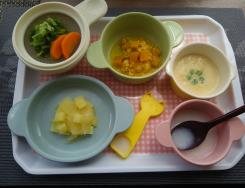 トレイにライスがゆ、にんじんとキャベツのスープ煮、とりわけクリーミースープなどの6種類の離乳食が並べられている写真