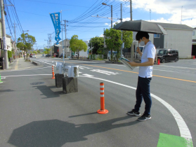 道路に設置されたラバーポールを日傘をさしながら確認している男性の写真