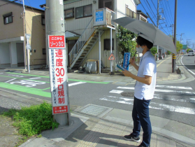 電柱に掛けてある看板を日傘をさしながら確認している男性の写真