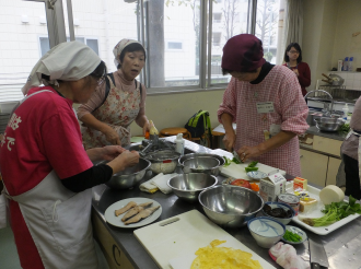 調理台に様々な食材や調理道具が置かれ、3人の女性が調理をしている写真