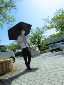 晴天の下、男性が日傘をさしてカゴを持ち、歩道を歩いている写真