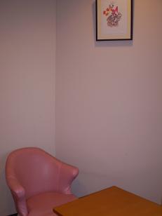 壁に額縁に入った絵が飾られており、ピンクの椅子と木の机が置かれている写真