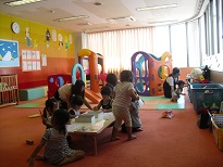 中央に遊具、周りに籠などで整頓された室内で数組の親子が遊んでいるひよこサロンの様子を写した写真